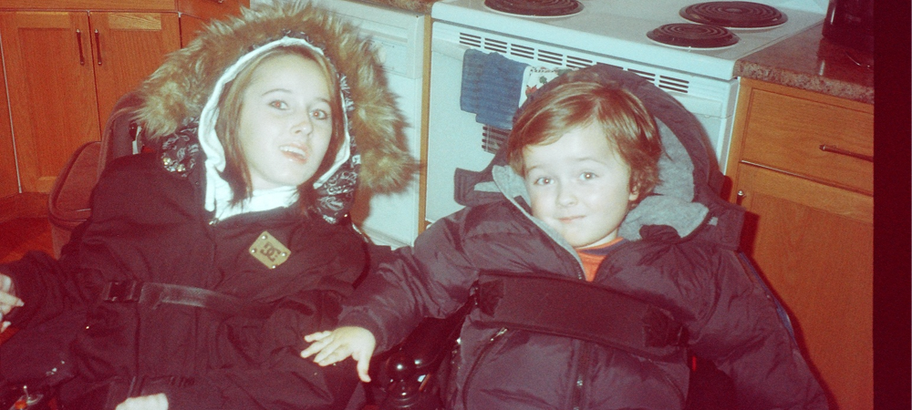 Karli and her brother sitting in kitchen wearing winter coats