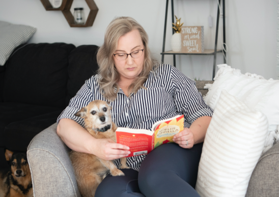 Woman with dogs reading book on sofa