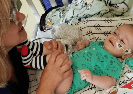 baby laying in crib and smiling while a woman looks down on him while holding baby’s feet