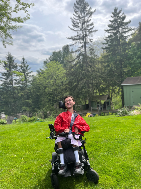 Jeune homme en fauteuil roulant portant un manteau rouge et souriant à l’extérieur dans une cours arrière