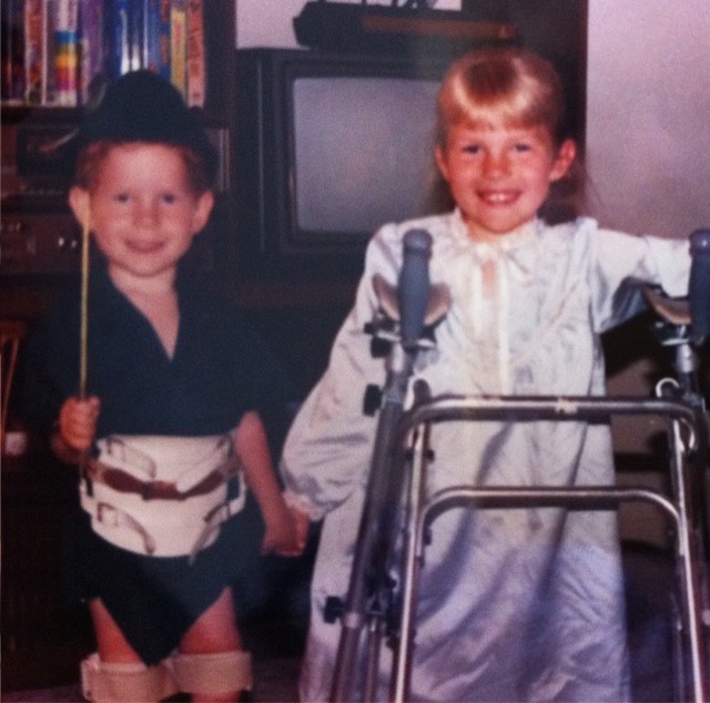 A photo of Kevan and his sister as toddlers, holding hands and smiling at the camera. Both Kevan and his sister have SMA Type 2.