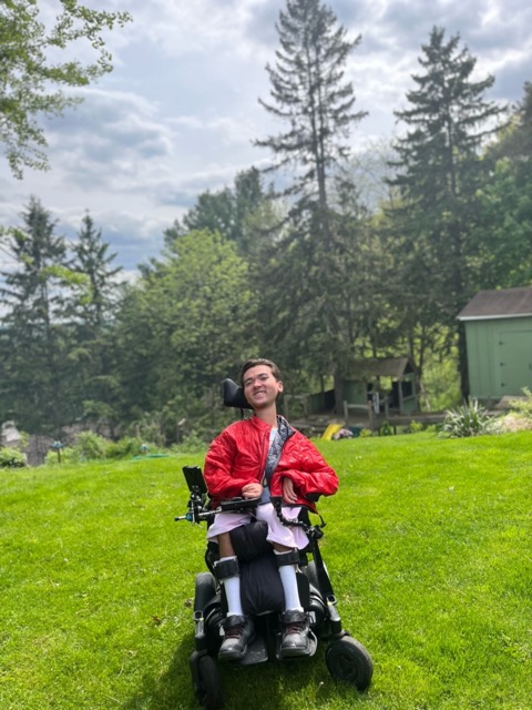 Young man in wheelchair wearing red jacket sitting outside home on outdoor stone landing