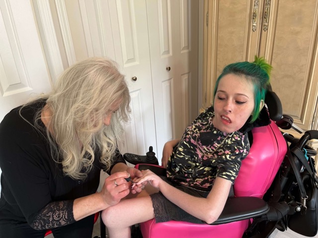 Femme blonde qui applique du vernis à ongle à une patiente atteinte d’AS dans un fauteuil roulant