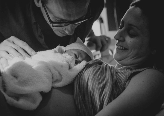 Photo en noir et blanc de Maude et de son mari avec un nouveau-né contre elle.