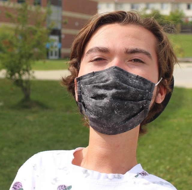 Gros plan sur le visage d’un jeune homme, qui porte un masque chirurgical noir.